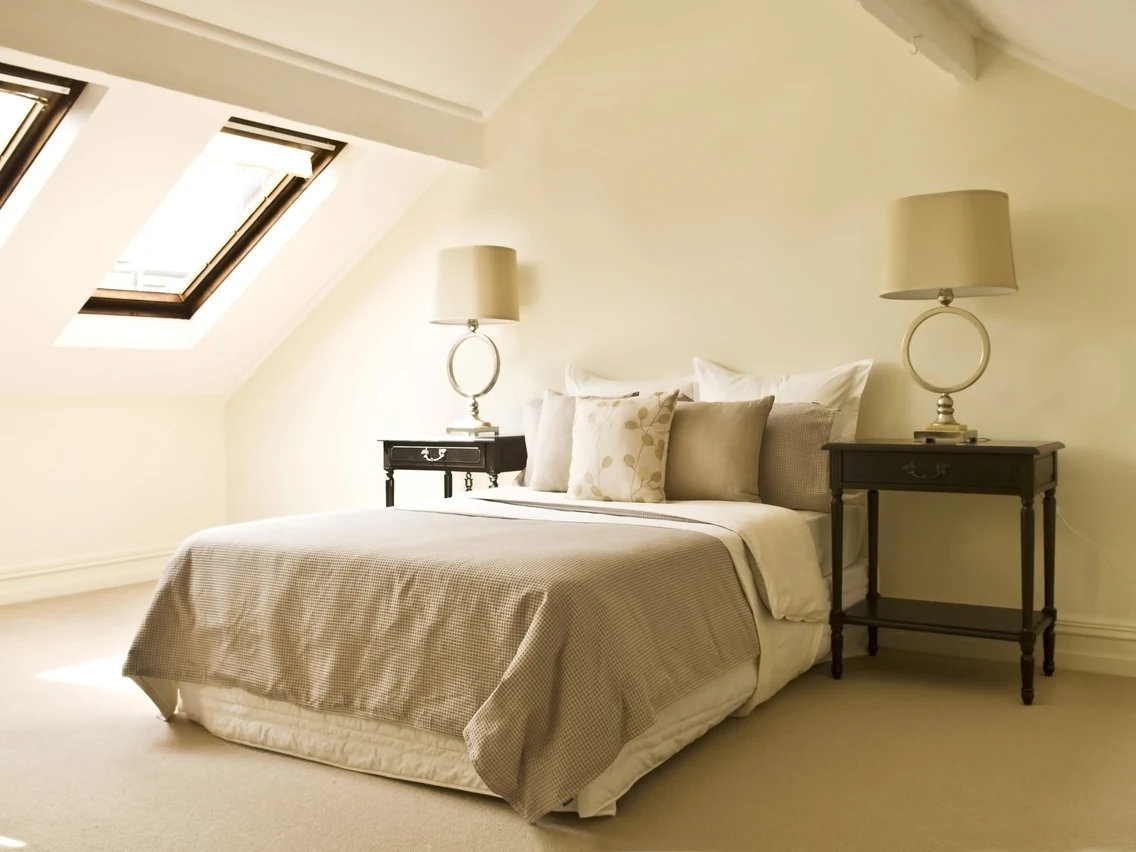 Loft bedroom with cream painted walls, exposed beams, and skylight in Preston by Rose Decor